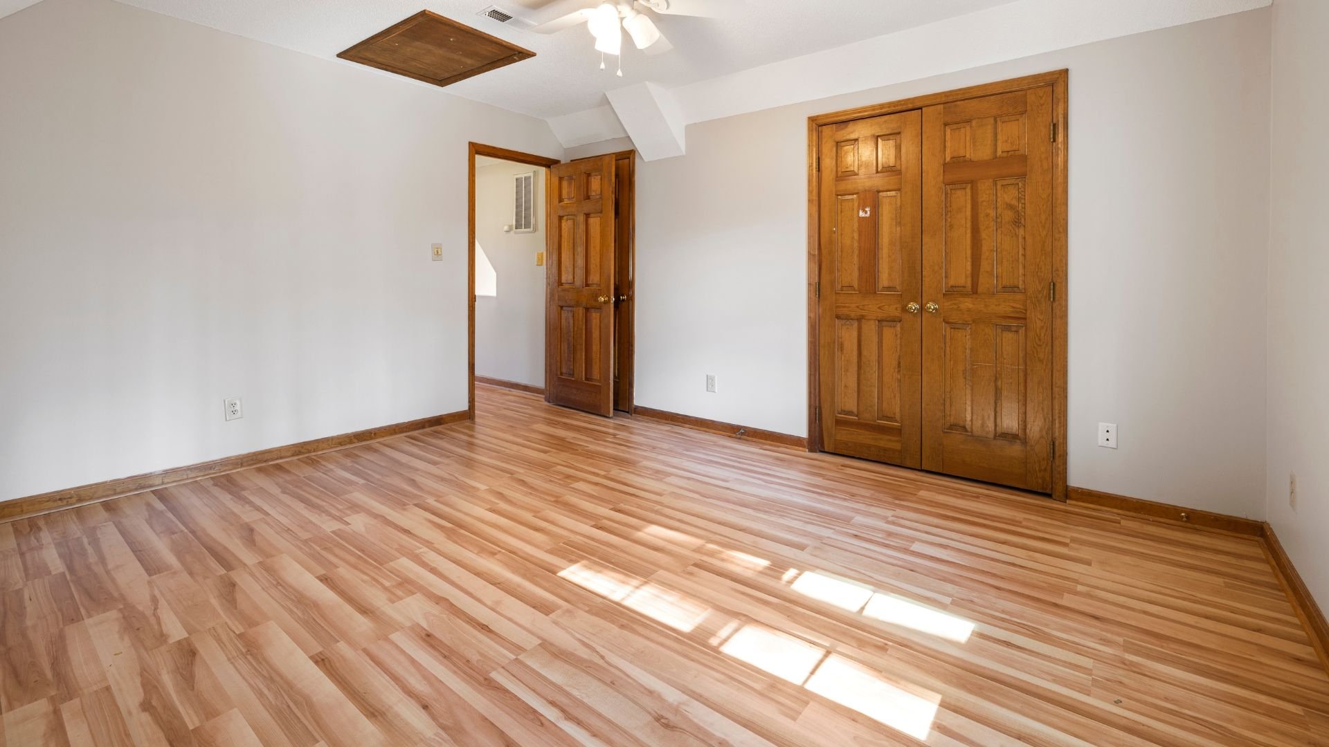 Empty room with wooden floor, white walls, and wooden panel doors