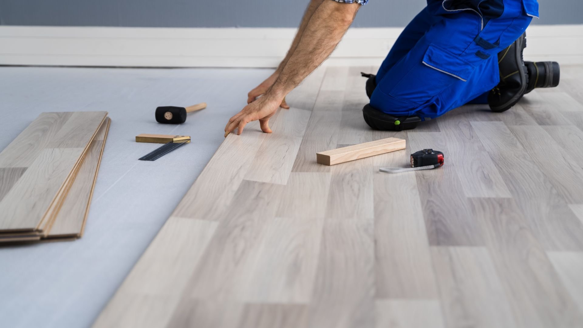 Person installing laminate flooring with tools and measuring equipment
