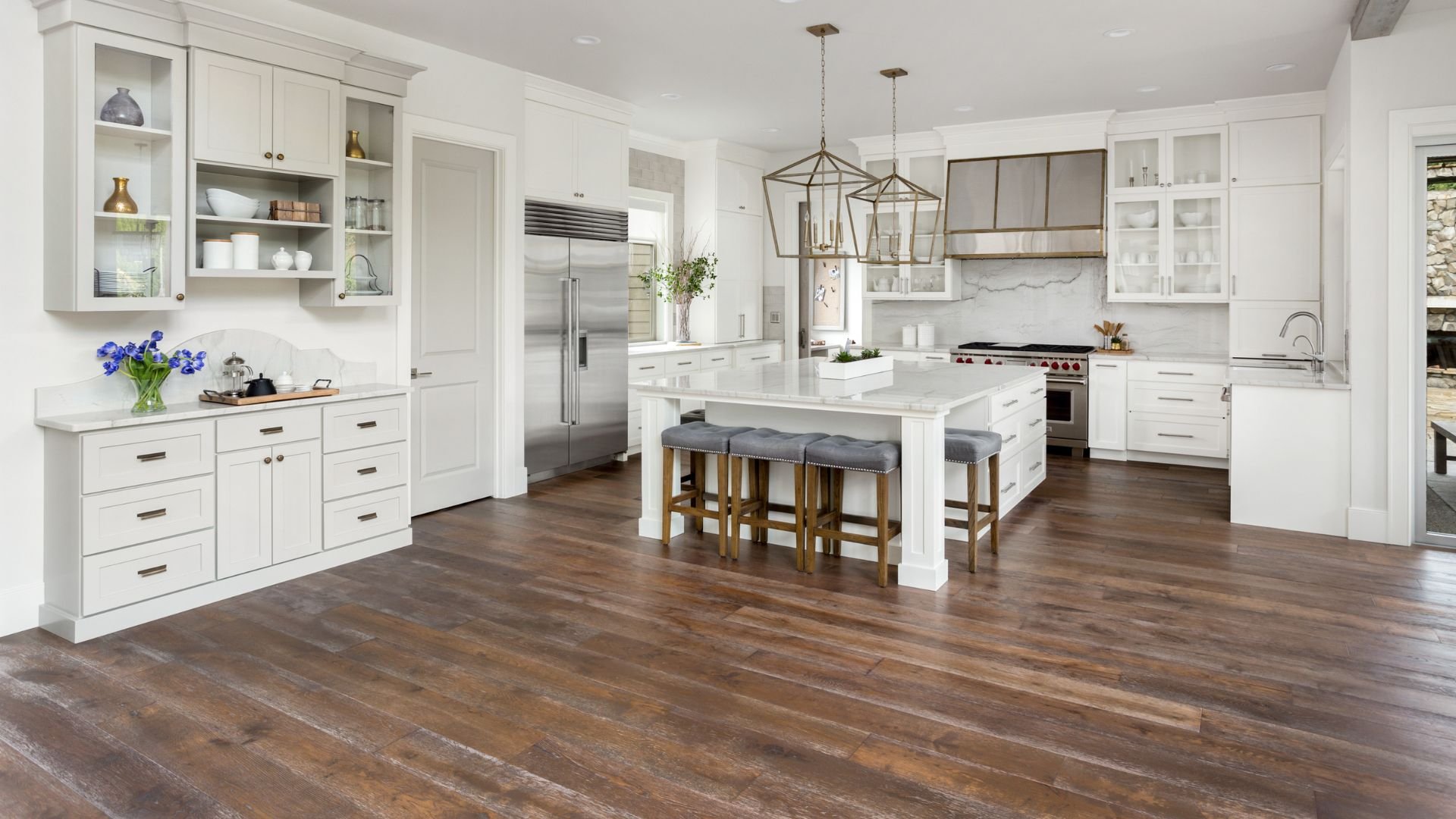 Spacious white kitchen with wood floors, island, and hanging pendant lights